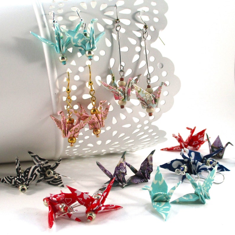 Op de afbeelding: Een paar origami-kraanvogel-oorbellen gemaakt van gepatenteerd papier. De oorbellen zijn verkrijgbaar in verschillende kleuren en patronen, waaronder blauw, roze, rood en zwart. De oorbellen zijn perfect om elke outfit een vleugje speelsheid te geven.