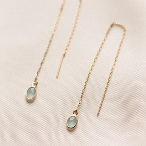 Peut inclure: Une paire de boucles d'oreilles pendantes en or. Chaque boucle d'oreille est ornée d'une petite pierre précieuse ovale vert pâle suspendue à une fine chaîne en or. Les boucles d'oreilles sont présentées sur un fond blanc cassé.
