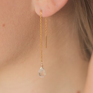 May include: Gold chain earrings with a clear teardrop-shaped gemstone hanging from the end of each chain.