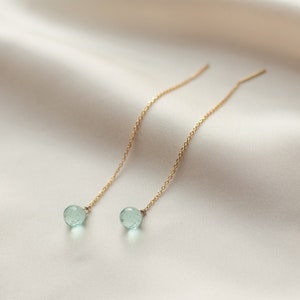 Może przedstawiać: Para delikatnych złotych kolczyków z łańcuszkiem i jasnoniebieskimi kamieniami.