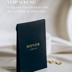 May include: A black gift box with gold lettering that reads "HONOR JEWELRY". The box is on a white surface.