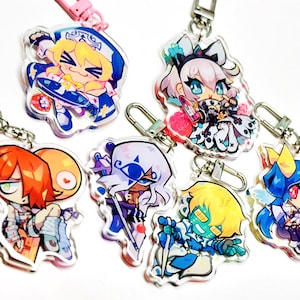 May include: Six clear acrylic keychains featuring colourful anime-style character illustrations. Each charm includes a metal lobster clasp. The designs depict various figures with distinct hair colours, outfits, and accessories in a vibrant, cartoon aesthetic.