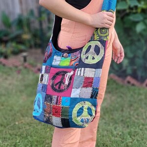 Puede incluir: Una mujer lleva un mono de color melocotón y una camiseta negra y lleva un bolso de hombro de patchwork con símbolos de paz. El bolso está hecho de diferentes telas y colores, incluyendo azul, verde, rojo y blanco.