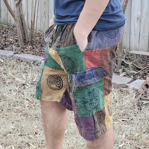 Peut inclure: Shorts patchwork multicolores avec divers motifs géométriques et floraux. Les shorts ont une coupe décontractée et des poches. La personne porte des sandales noires. Les shorts sont faits d'une matière douce et confortable.