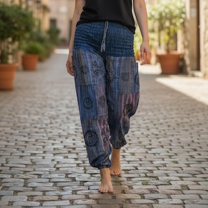 Op de afbeelding: Een zwart T-shirt met korte mouwen gecombineerd met een losvallende blauwe broek met een gesmokte elastische tailleband met trekkoord en een donkerblauw, paars en grijs patchworkpatroon met cirkelvormige zwarte bloemmotieven.