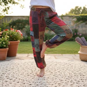 May include: Patchwork trousers featuring a multi-colored design with red, blue, and brown rectangular panels. The pants include a drawstring waistband, elasticized cuffs at the ankles, and black circular patterns printed across the fabric surface.