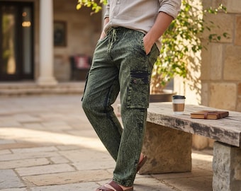 May include: Olive green cargo pants featuring a dark, mottled, leaf-like pattern throughout. The pants include a drawstring waistband, side pockets, and a distinct black flap pocket on the thigh. The fabric has a textured appearance with a straight leg cut.