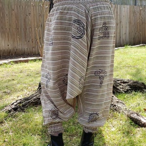 May include: Beige and brown striped pants with a wide elastic waistband and black printed designs. The pants are gathered at the ankles.