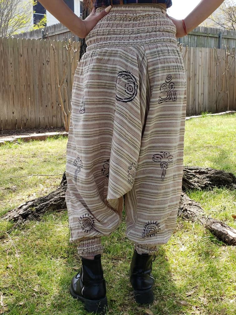 May include: Beige and brown striped pants with a wide elastic waistband and black printed designs. The pants are gathered at the ankles.