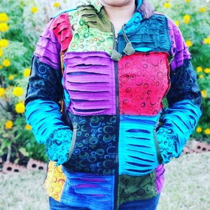 Może przedstawiać: Kolorowa kurtka w stylu patchwork z zamkiem błyskawicznym i kapturem. Kurtka jest wykonana z różnych tkanin z wzorem w kółka i ma przetarte detale.