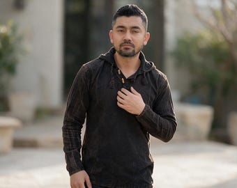 May include: A long-sleeved, dark brown hooded pullover shirt featuring a textured, slightly faded fabric finish. The garment includes a hood with drawstring cords and a partial front placket with two small, light-colored wooden toggle buttons.