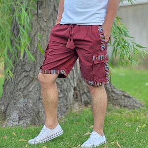 May include: Burgundy cargo shorts with colorful patterned trim and pockets. The shorts have a drawstring waist and are worn with white sneakers. The shorts are knee-length and appear to be made of a lightweight fabric.