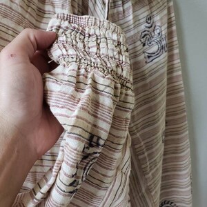 May include: A white and brown striped top with a gathered elastic neckline and long sleeves. The top has a brown and black printed design with a symbol that looks like an Om.