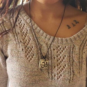 May include: A black cord necklace with a square pendant featuring the Om symbol in black and white. The pendant is made of ceramic and has a slightly textured surface.