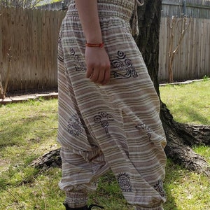 May include: Beige and brown striped pants with a drawstring waist and black and white patterned designs. The pants are loose fitting and have a wide leg.