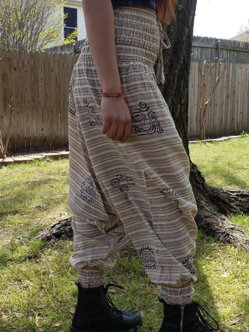 May include: Beige and brown striped pants with a drawstring waist and black and white patterned designs. The pants are loose fitting and have a wide leg.