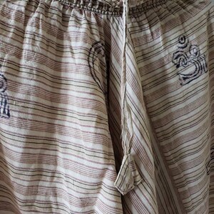 May include: White and brown striped cotton pants with a drawstring waist and a small tassel. The pants have a subtle pattern of small, dark brown symbols.