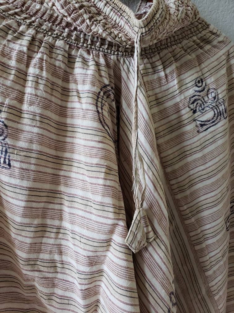 May include: White and brown striped cotton pants with a drawstring waist and a small tassel. The pants have a subtle pattern of small, dark brown symbols.