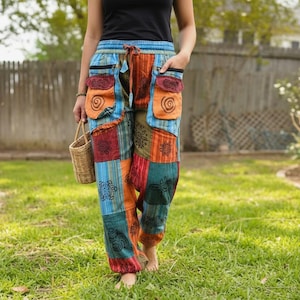 Può includere: Pantaloni patchwork dal taglio ampio caratterizzati da un mix vivace di pannelli in tessuto blu, arancione, rosso e verde. I pantaloni presentano una vita elastica con coulisse, due ampie tasche frontali con chiusura a patta e stampe a spirale.