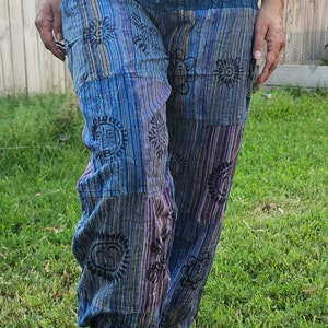 May include: Blue and purple striped pants with a patchwork design and black sun-like patterns. The pants are gathered at the waist and have a drawstring.