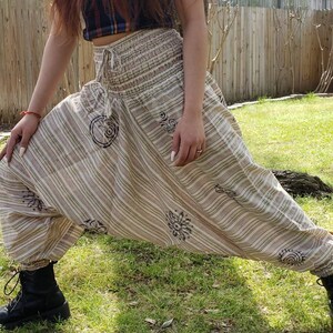 May include: A pair of striped, cream-colored pants with a brown elastic waistband and a drawstring. The pants have a loose, flowing fit and feature a unique design with brown circular patterns.