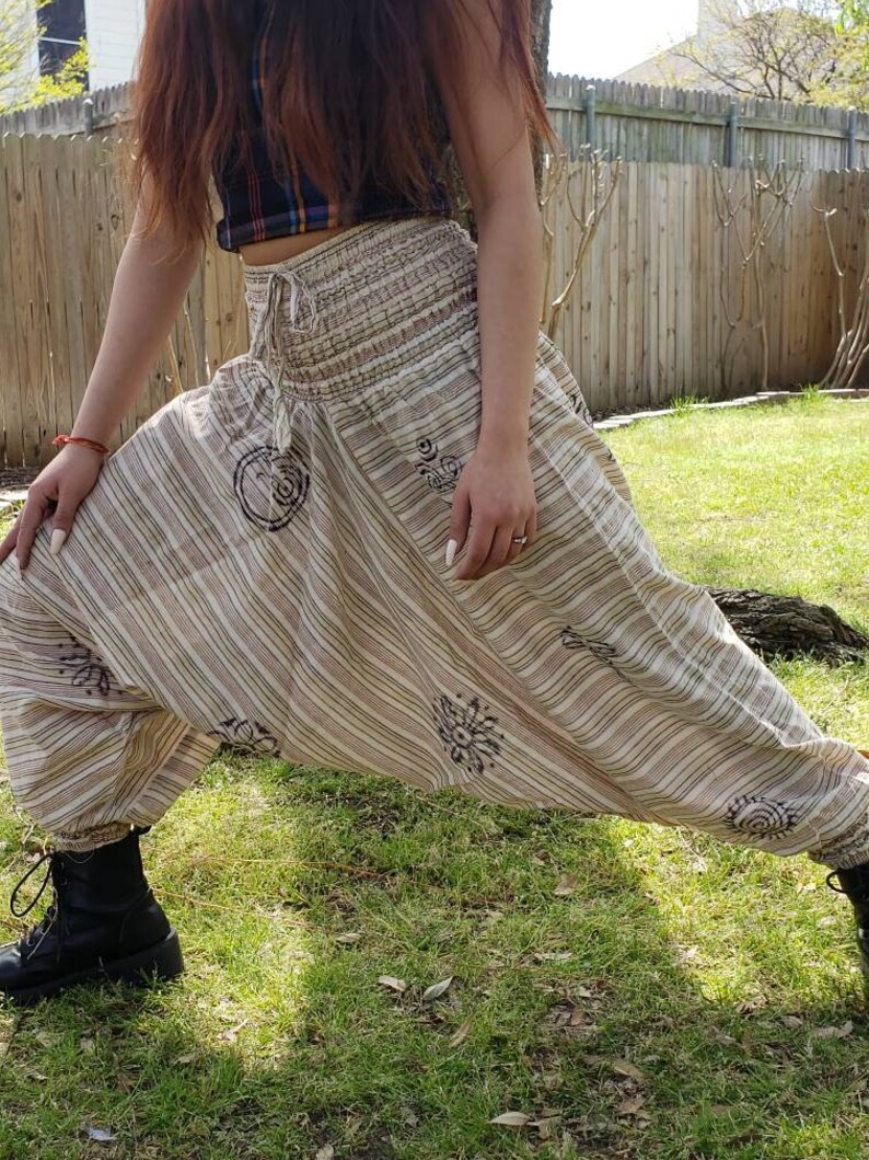 May include: A pair of striped, cream-colored pants with a brown elastic waistband and a drawstring. The pants have a loose, flowing fit and feature a unique design with brown circular patterns.