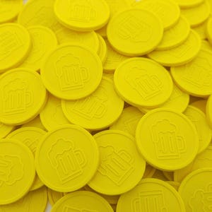 Puede incluir: Un montón de fichas redondas de color amarillo brillante con una imagen en relieve de una jarra de cerveza en cada ficha.
