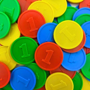 Puede incluir: Un conjunto de fichas de juego redondas y coloridas. Las fichas son rojas, verdes, azules y amarillas, cada una con el número "1" en relieve. Las fichas están dispersas, creando una imagen vibrante y lúdica.