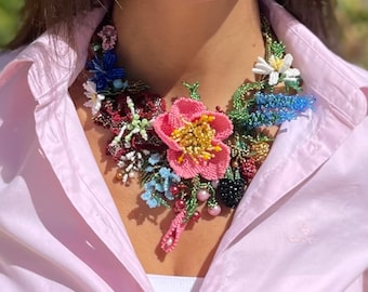 Könnte beinhalten: Eine bunte Perlenkette mit Blumen in Rosa, Rot, Blau, Grün und Weiß. Die Kette ist aus Perlen und Draht gefertigt und soll wie ein Blumenstrauß aussehen.