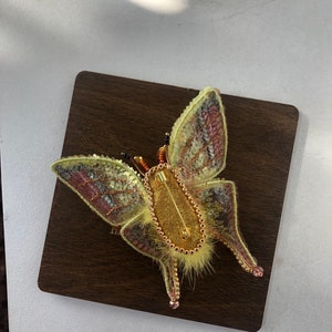 May include: A yellow and pink beaded butterfly brooch with a gold pin and a furry body.