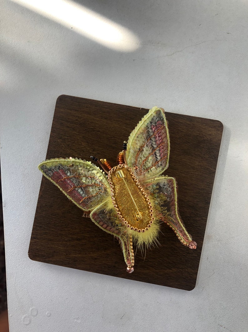 May include: A yellow and pink beaded butterfly brooch with a gold pin and a furry body.