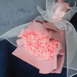 May include: A bouquet of pink hydrangeas wrapped in pink tissue paper and white netting.