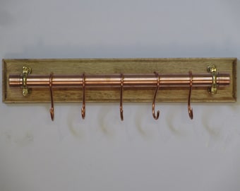 Copper kitchen utensil/pan hanging rail mounted on a wooden back board with handmade solid copper hanging hooks.