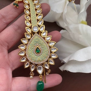 以下が含まれることがあります： 緑と白のエナメルデザインの金色のヘアクリップ。クリップはクリアなラインストーンと緑色の宝石で飾られています。