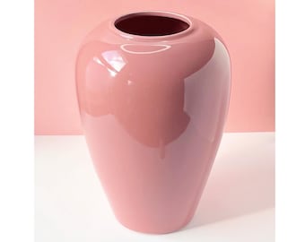 May include: A glossy, light pink ceramic vase with a rounded, oval shape.