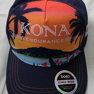 May include: Navy blue trucker hat with a sunset graphic featuring palm trees and the word "KONA ENDURANCE". The hat has a curved brim and a perforated top for breathability. Includes a snapback closure.