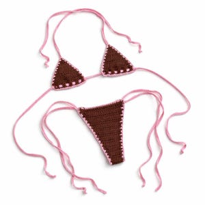 May include: A brown crochet bikini set with pink trim and ties. The triangle top and thong-style bottoms are handmade. The bikini is displayed on a white background.