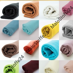 Könnte beinhalten: Eine Sammlung von 12 Stoffrollen in verschiedenen Farben, darunter Schwarz, Braun, Beige, Hellblau, Türkis, Orange, Gelb, Grau, Rosa, Rotbraun, Grün und Creme. Die Stoffrollen sind alle aufgerollt und mit einem Band gebunden.