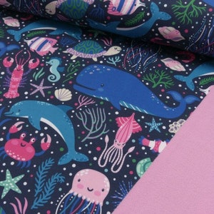 May include: A dark blue fabric with a repeating pattern of sea creatures. The pattern includes whales, dolphins, jellyfish, seahorses, starfish, crabs, and seaweed. The fabric is perfect for crafting projects, quilting, and sewing.
