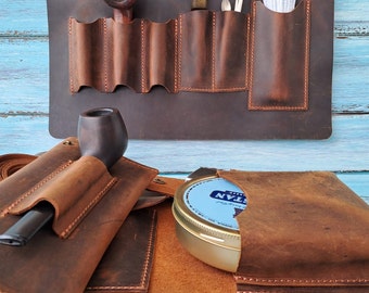 May include: A brown leather tobacco pouch with multiple pockets and compartments. The pouch is open to reveal a round tin of pipe tobacco. The pouch is made of distressed leather and has a rustic look.