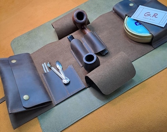 May include: A brown leather pipe tobacco pouch with a separate pouch for a pipe, a small tin, and a variety of tools. The pouch is open and laid flat, revealing the contents. The pouch has a G.R. label on the outside.