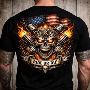 May include: Black t-shirt featuring a skull design with pistons, flames, and an American flag. The phrase "RIDE OR DIE" is displayed on a banner below the skull. A small skull is below the banner.
