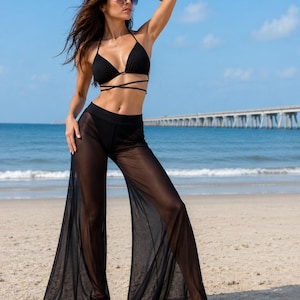 May include: A black bikini top with thin straps that wrap around the torso, paired with matching black bikini bottoms and sheer, wide-leg, floor-length mesh trousers. The set is solid black and features a lightweight, semi-transparent fabric.