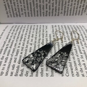 May include: A pair of black triangle-shaped earrings with silver glitter embedded in the resin. The earrings have silver hooks.