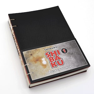 May include: Black leather-bound notebook with a red and white title page that says "Shibaku 1 Basis & Grundlagen".