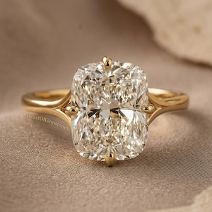 Puede incluir: Un anillo de compromiso de oro con un gran diamante de talla rectangular. El diamante transparente y brillante está engastado en una delicada banda de oro. El anillo se muestra sobre una tela de tono neutro.