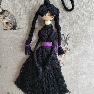 May include: A black yarn doll with long black hair, a purple ribbon around the waist, and a wooden bead head.