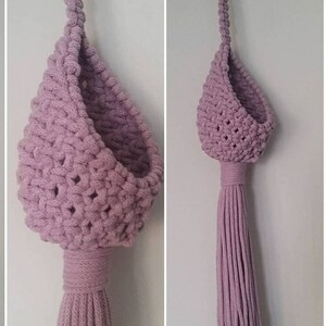 May include: A light purple macrame hanging planter with a tassel. The planter is made of thick cotton cord and has a rounded, teardrop shape.