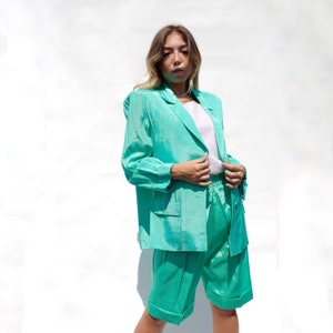 May include: A teal green blazer and matching shorts set. The blazer has a single button closure and a pocket on each side. The shorts have a wide leg and a cuffed hem.