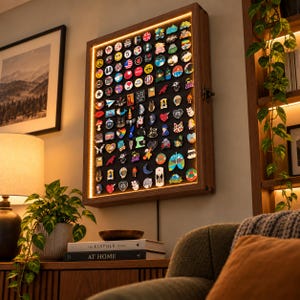 May include: A rectangular wooden wall-mounted display case with integrated LED lighting, featuring a black interior backing filled with a large collection of assorted colorful enamel pins in various shapes, sizes, and graphic designs.